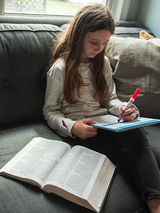 Girl reading the Bible and completing an interactive worksheet.